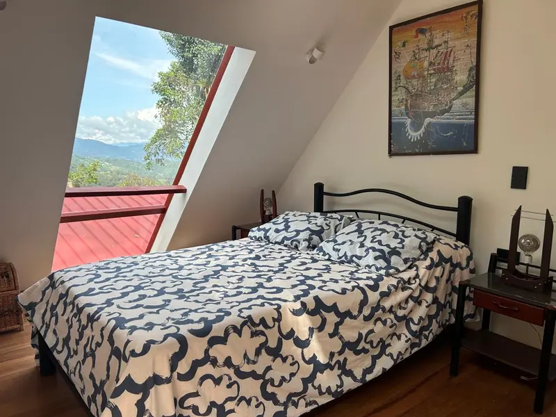 Habitación con cama doble y ventana inclinada con vista a las montañas