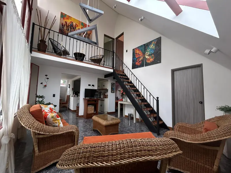 Sala del chalet con muebles de mimbre, escalera y balcón interior
